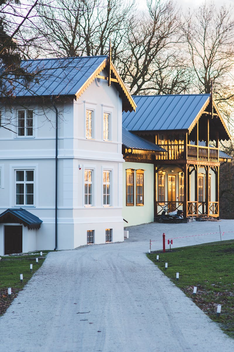 White mansion with a garden and driveway at sunset, showcasing elegant architecture.